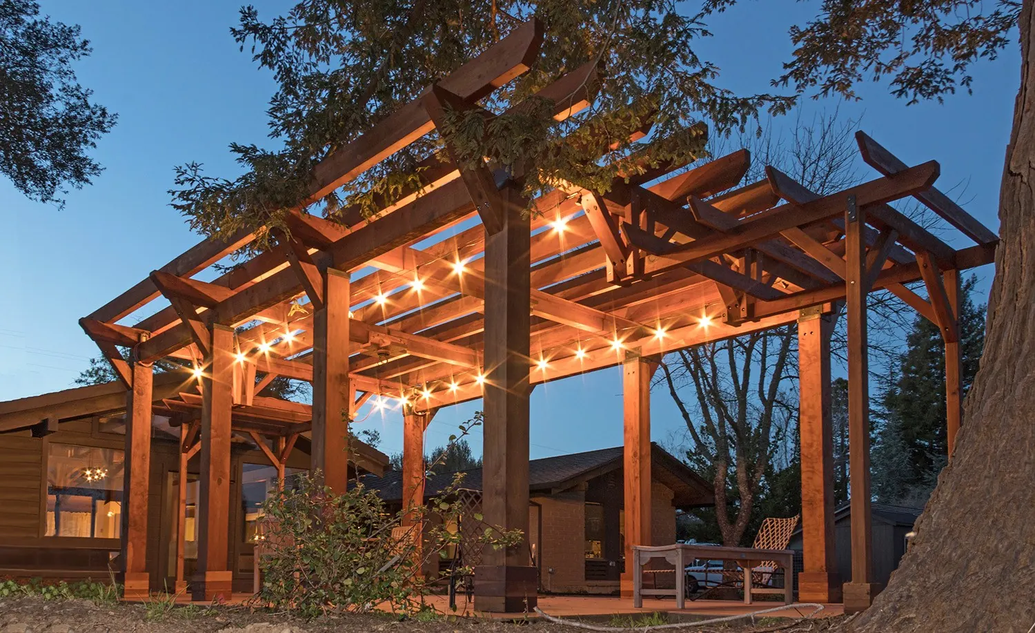 Custom redwood pergola lit with string lights at dusk