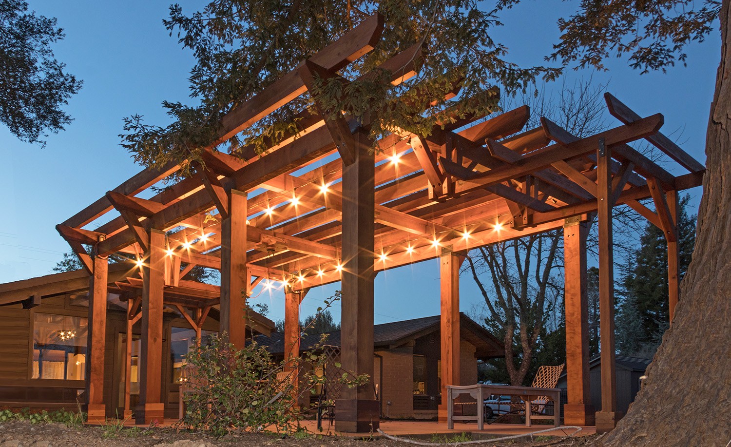 Custom redwood pergola lit with string lights at dusk
