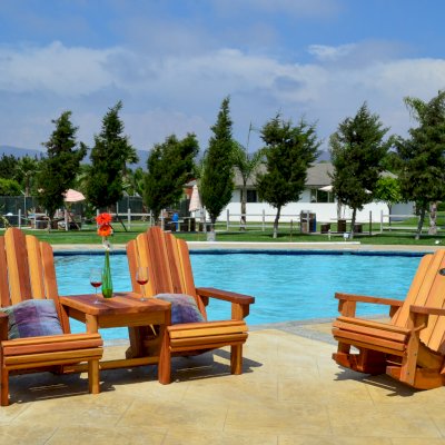 Adirondack Vignette Settee (Options: Standard Width, California Redwood, Slightly Rounded Corners, Umbrella Hole, Standard Seat Depth, Custom Cushion, No Ottoman, Transparent Premium Sealant). Photo also shows an Adirondack Rocking Chair. Rocker built in Douglas-Fir with Transparent Premium Sealant.