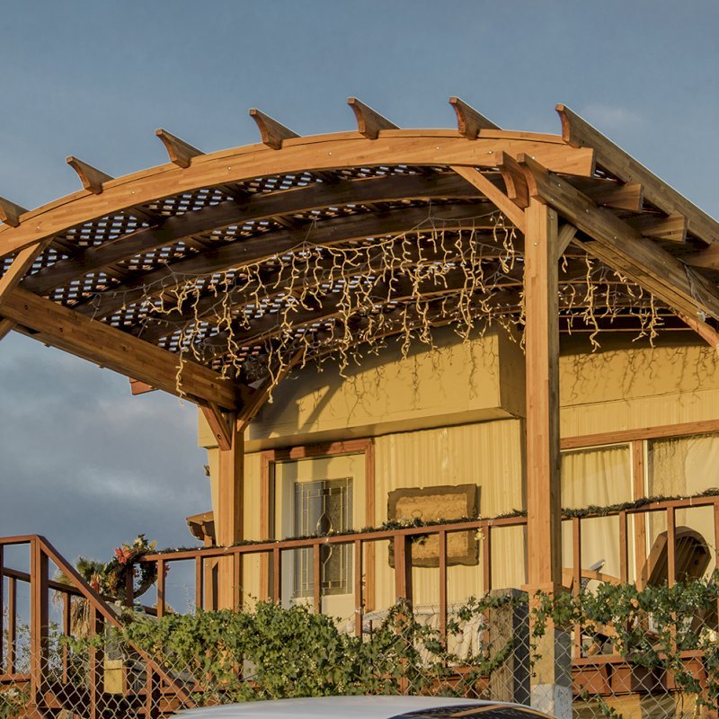 Arched Pergola Kit (Options: 12' L x 16' Arc W, Mosaic Eco-Wood, No Electrical Wiring Trim Kit, 4 Post Anchor Kit for Wood, No Ceiling Fan Bases, No Privacy Panels, No Curtain Rods, 9' Post Height, Transparent Premium Sealant). Free Standing Pergola was altered slightly to place up against house by limiting overhang on house side. Arched Pergola Kit (Options: 12' L x 16' Arc W, Mosaic Eco-Wood, No Electrical Wiring Trim Kit, 4 Post Anchor Kit for Wood, No Ceiling Fan Bases, No Privacy Panels, No Curtain Rods, 9' Post Height, Transparent Premium Sealant). Free Standing Pergola was altered slightly to place up against house by limiting overhang on house side.
