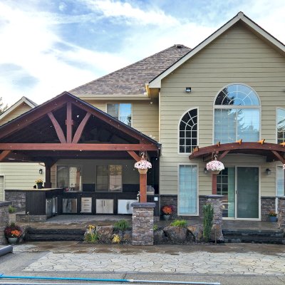 Del Norte Outdoor Kitchen Pavilion (Options: 19.5' L x 17' W, Mature Redwood, No Privacy Panel, Post Anchor Kit for High Wind, 10.5' H Posts, 1 Ceiling Fan Base, Electrical Wiring Trim for 2 Posts, No Curtain Rod, Coffee-Stain Premium Sealant). Photo Also Shows a 12' x 12' Attached Arched Pergola. Photo Courtesy of Elements Landscaping of Hayden, ID.