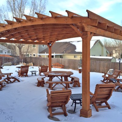 Ensenada Wooden Rocking Chair (Options: Standard Width, Mature Redwood, No Cushion,Transparent Premium Sealant). Photo Also Shows an Arched Pergola, a Round Picnic Table Set, 4 Ensenada Easychairs with Ottomans and a Lutyens Bench in Background. Photo Courtesy of Mike Budzinak of Cheyenne, Wyoming.