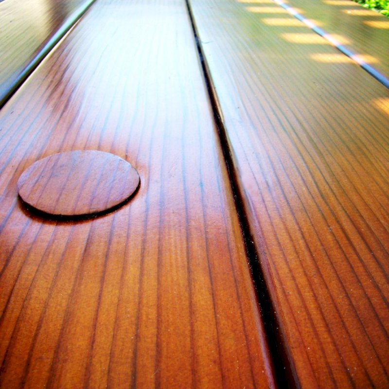 Closeup of tabletop highlighting the quality of the vertical grain lumber and the Transparent Premium Sealant - Mature Redwood. Umbrella hole and plug is shown on top left. Closeup of tabletop highlighting the quality of the vertical grain lumber and the Transparent Premium Sealant - Mature Redwood. Umbrella hole and plug is shown on top left.