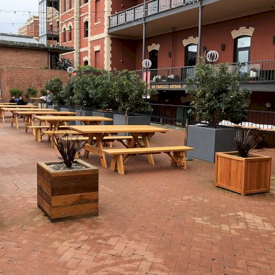 Forever Picnic Tables (Unattached Benches) (Options: 7' L, 34 ½in W, Some Table with No Seating and Some with Side Benches, Douglas-fir,1 Full Length Side Bench Per Side, Standard Tabletop, Slightly Rounded Corners, No Umbrella Hole, Transparent Premium Sealant). Photo also shows some Mendocino and Napa Planters. Photo Courtesy of A. Frost. Installed at Ghirardelli Square, West Plaza Beer Garden, located at 900 North Point Street at the corner of Beach & Larkin Streets, San Francisco, CA.
