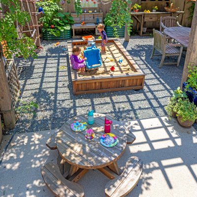 La Playa Sandbox (Options: 96"L x 60" W x 15" H, Mosaic Eco-Wood, Tongue and Grooved Lid, Transparent Premium Sealant). Photo Also Shows a Round Wooden Picnic Table for Toddlers. Photo Courtesy of M. Cooke of Westchester, IL.