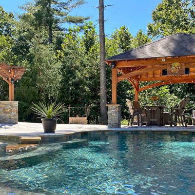 Marin Outdoor Kitchen Pergola (Options: 14' L x 15' Arc W, Douglas-fir, Unattached, 1 Post Electrical Wiring Trim, 4-Post Anchor Kit for High-Wind, No Ceiling Fan Base, No Privacy, No Curtain Rods, 9.5 ft Post Height (posts wrapped with masonry), Transparent Premium Sealant). Photo Also Shows a Loreto Pavilion. Photo Courtesy of Bill & Lori O’Mara of Marion, North Carolina.