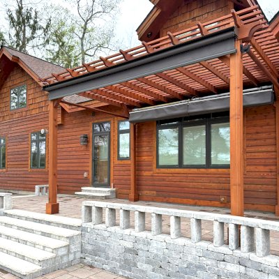 Traditional Wooden Garden Pergola (Options: 17' L x 12.5' W, Mature Redwood, Electrical Wiring Trim for 1 Post, Open Roof with Slats at 6", Rafters at 18", Post Anchor Kit for Stone, No Post Decorative Trims, No Ceiling Fan Base, No Privacy Panels, 2 Curtain Rods & Stainless Steel Hangers, 11' Posts, Transparent Premium Sealant). Photo Courtesy of A. Kipela of Iron Mountain, MI.