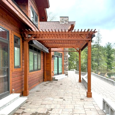 Traditional Wooden Garden Pergola (Options: 17' L x 12.5' W, Mature Redwood, Electrical Wiring Trim for 1 Post, Open Roof with Slats at 6", Rafters at 18", Post Anchor Kit for Stone, No Post Decorative Trims, No Ceiling Fan Base, No Privacy Panels, 2 Curtain Rods & Stainless Steel Hangers, 11' Posts, Transparent Premium Sealant). Photo Courtesy of A. Kipela of Iron Mountain, MI.