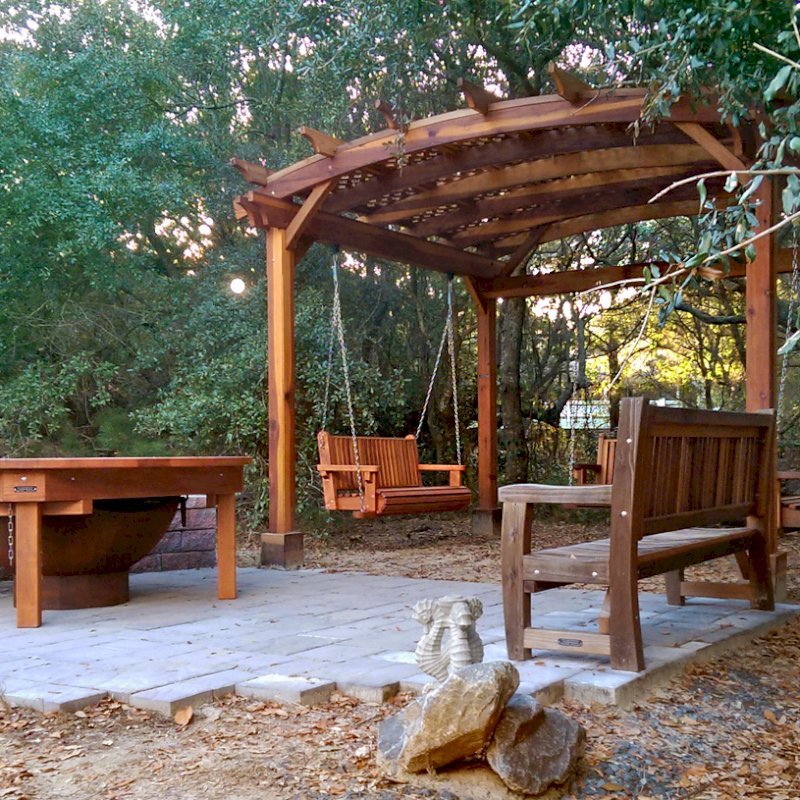 Round Patio Table (Options: 6.5 ft, No Seating, Redwood, Standard Tabletop, No Lazy Susan, No Umbrella Hole, Transparent Premium Sealant, Braces Underneath Tabletop by Custom Request). Photo Also Shows an Arched Pergola with 3 Bench Swings and a Ti Amo Bench. Photo Courtesy of Tom Marten of Kitty Hawk, NC. Round Patio Table (Options: 6.5 ft, No Seating, Redwood, Standard Tabletop, No Lazy Susan, No Umbrella Hole, Transparent Premium Sealant, Braces Underneath Tabletop by Custom Request). Photo Also Shows an Arched Pergola with 3 Bench Swings and a Ti Amo Bench. Photo Courtesy of Tom Marten of Kitty Hawk, NC.