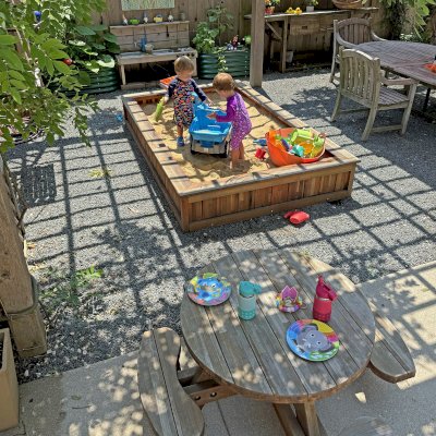 Round Wooden Picnic Table for Toddlers (Mosaic Eco-Wood, No Umbrella Hole, Standard Tabletop, Transparent Premium Sealant). Photo Also Shows a La Playa Sandbox and an Eli's Potting Bench. Photo Courtesy of M. Cooke of Westchester, IL.