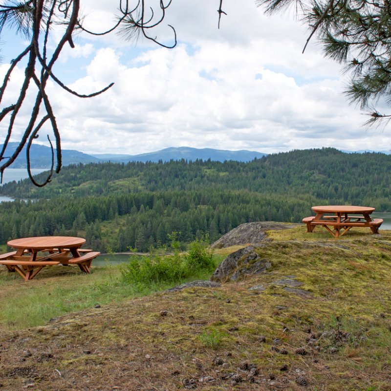 Round Wooden Picnic Tables (Attached Benches) (Options: 6' Diameter, Attached Benches, Redwood, Standard Tabletop, No Lazy Susan, Umbrella Hole & Plug, Transparent Premium Sealant). These beautiful tables are installed at the “Bull Pine Ledge”, looking out on Lake Pend Orielle from Cloudsledge Conservation Trust, Hope Idaho. Photo Courtesy of Art Green. Round Wooden Picnic Tables (Attached Benches) (Options: 6' Diameter, Attached Benches, Redwood, Standard Tabletop, No Lazy Susan, Umbrella Hole & Plug, Transparent Premium Sealant). These beautiful tables are installed at the “Bull Pine Ledge”, looking out on Lake Pend Orielle from Cloudsledge Conservation Trust, Hope Idaho. Photo Courtesy of Art Green.