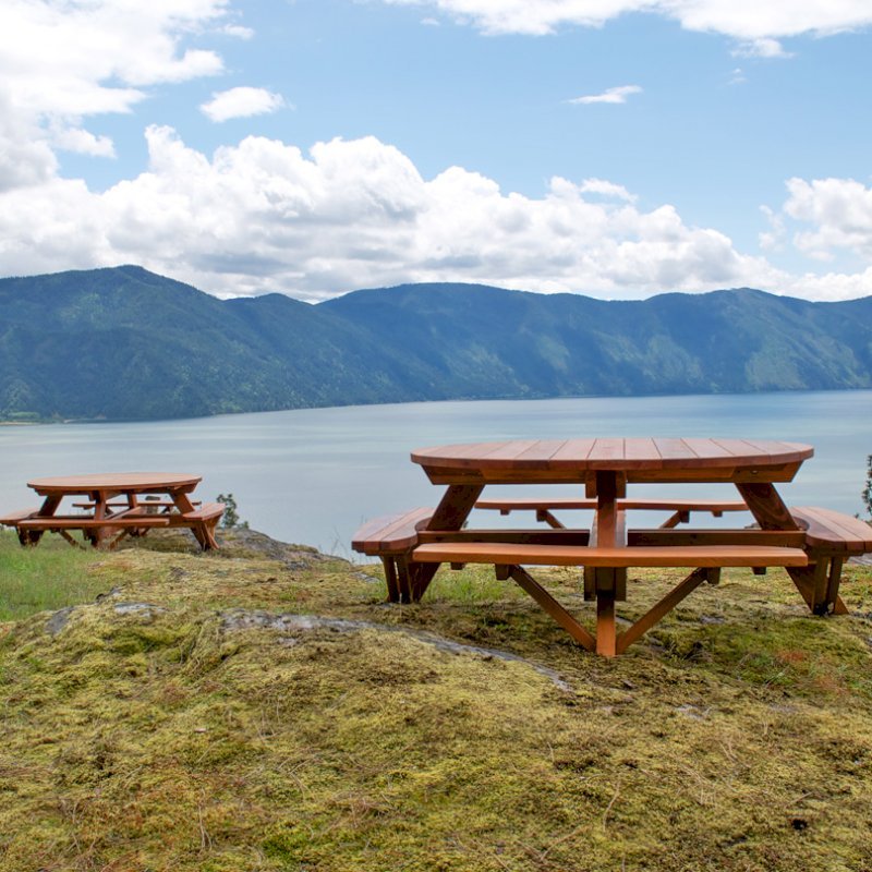 Round Wooden Picnic Tables (Attached Benches) (Options: 6' Diameter, Attached Benches, Redwood, Standard Tabletop, No Lazy Susan, Umbrella Hole & Plug, Transparent Premium Sealant). These beautiful tables are installed at the “Bull Pine Ledge”, looking out on Lake Pend Orielle from Cloudsledge Conservation Trust, Hope Idaho. Photo Courtesy of Art Green. Round Wooden Picnic Tables (Attached Benches) (Options: 6' Diameter, Attached Benches, Redwood, Standard Tabletop, No Lazy Susan, Umbrella Hole & Plug, Transparent Premium Sealant). These beautiful tables are installed at the “Bull Pine Ledge”, looking out on Lake Pend Orielle from Cloudsledge Conservation Trust, Hope Idaho. Photo Courtesy of Art Green.