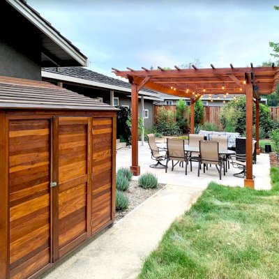 Storage Sheds (Options: 7' W, 4.5' D, 7' H, California Redwood, Single Door, One Shelf on the Side Opposite the Door, 42" H, Transparent Premium Sealant). Photo Also Shows a Garden Pergola in the Background. Photo Courtesy of J. Lewis of Mountain View, CA.