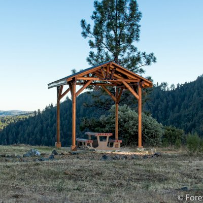 Humboldt Log Pavilion (Options: 6in x 6in Posts Thickness, 12ft L x 12ft W, No Privacy Panels, California Redwood, 2 Fascia Boards for Gutters, 9.5ft Post Height, No Electrical Wiring Trim, 4-Post Anchor Kit for High-Wind, No Ceiling Fan Fan Bases, No Curtain Rods, Transparent Premium Sealant). Metal Roof Installed by Custom Request.