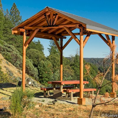 The Humboldt Log Pavilion (Options: 6in x 6in Posts Thickness, 12ft L x 12ft W, No Privacy Panels, California Redwood, 2 Fascia Boards for Gutters, 9.5ft Post Height, No Electrical Wiring Trim, 4-Post Anchor Kit for High-Wind, No Ceiling Fan Fan Bases, No Curtain Rods, Transparent Premium Sealant). Metal Roof Installed by Custom Request.