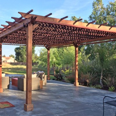 Lattice Pergola Kit (Options: 25' L x 18' W, California Redwood, No Electrical Wiring Trim, Lengthwise Roof Support Timbers, 6-Post Anchor Kit for Concrete, No ceiling Fan Base, No Privacy Panels, 4 Curtains Rods, 9.5' Post Height, Transparent Premium Sealant). 2x2 Slats Above Rafters was Added as Custom Detail. It is not Part of Standard Design. Photo Courtesy of Tom Deckowski of Morgan Hill, CA. Note that photo shows 2 yr old finish that is partially faded.