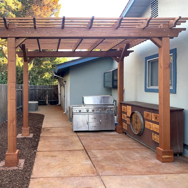 The Traditional Wooden Garden Pergola (Options: 12' L x 10' W, California Redwood, No Electrical Wiring Trim, Open Roof with Slats at 6", Rafters at 18", 4-Post Anchor Kit for Concrete, No Ceiling Fan Base, No Privacy Panels, No Curtain Rods, 9.5' Posts, Transparent Premium Sealant). Photo Courtesy of C. Lowe of Davis, CA. The Traditional Wooden Garden Pergola (Options: 12' L x 10' W, California Redwood, No Electrical Wiring Trim, Open Roof with Slats at 6", Rafters at 18", 4-Post Anchor Kit for Concrete, No Ceiling Fan Base, No Privacy Panels, No Curtain Rods, 9.5' Posts, Transparent Premium Sealant). Photo Courtesy of C. Lowe of Davis, CA.