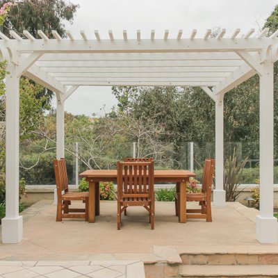 Traditional Wooden Garden Pergola (Options: 13' L x 12' W, Douglas-fir, 1 Electrical Wiring Trim, Open Roof with Slats at 6", Rafters at 18", 4-Post Anchor Kit for Concrete, No Ceiling Fan Base, No Privacy Panels, 1 Electrical Wiring Trim Kit, 9' Posts, Off-White Oil-Based Primer). Photo Also Shows a San Francisco Patio Table with Chairs in Mature Redwood. Photo Courtesy of J. Schulte of Laguna Niguel, CA.