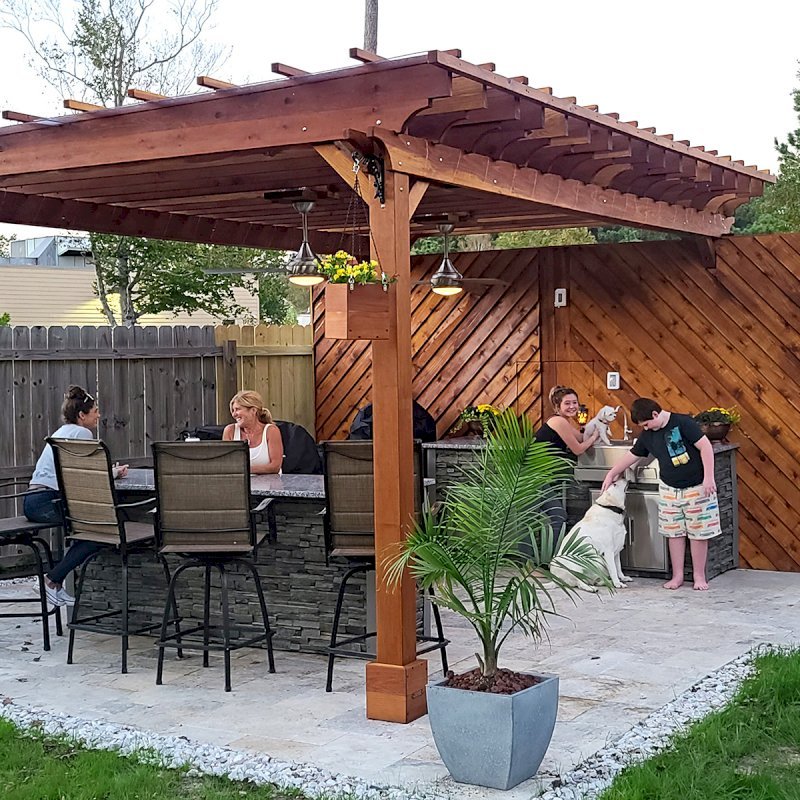 The Traditional Wooden Garden Pergola (Options: 18' L x 12' W, California Redwood, 1 Electrical Wiring Trim, Open Roof with Slats at 18", Rafters at 12" by Custom Request, with Rain Guard, 4-Post Anchor Kit for High-Wind, 2 Ceiling Fan Bases, No Privacy Panels, No Curtain Rods, 9.5' Posts, Transparent Premium Sealant). Rafters were designed with a slope for draining purpose. Photo Courtesy of M. McGourty of Virginia Beach, Virginia. The Traditional Wooden Garden Pergola (Options: 18' L x 12' W, California Redwood, 1 Electrical Wiring Trim, Open Roof with Slats at 18", Rafters at 12" by Custom Request, with Rain Guard, 4-Post Anchor Kit for High-Wind, 2 Ceiling Fan Bases, No Privacy Panels, No Curtain Rods, 9.5' Posts, Transparent Premium Sealant). Rafters were designed with a slope for draining purpose. Photo Courtesy of M. McGourty of Virginia Beach, Virginia.