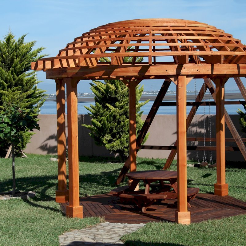The Wooden Dome Pergola (Options: 16' Diameter, with Deck in Coffee Stain, Douglas-fir, Open Roof with Slats at 6", 9' Posts, No Electrical Wiring Trim, 6-Post Anchor Kit for Concrete, Transparent Premium Sealant). Photo Also shows a Round Picnic Table and a Rory's Swing Set in Background. The Wooden Dome Pergola (Options: 16' Diameter, with Deck in Coffee Stain, Douglas-fir, Open Roof with Slats at 6", 9' Posts, No Electrical Wiring Trim, 6-Post Anchor Kit for Concrete, Transparent Premium Sealant). Photo Also shows a Round Picnic Table and a Rory's Swing Set in Background.