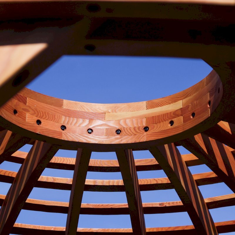The Wooden Dome Pergola (Options: 16' Diameter, with Deck in Coffee Stain, Douglas-fir, Open Roof with Slats at 6", 9' Posts, No Electrical Wiring Trim, 6-Post Anchor Kit for Concrete, Transparent Premium Sealant). Photo Also shows a Round Picnic Table and a Rory's Swing Set in Background. The Wooden Dome Pergola (Options: 16' Diameter, with Deck in Coffee Stain, Douglas-fir, Open Roof with Slats at 6", 9' Posts, No Electrical Wiring Trim, 6-Post Anchor Kit for Concrete, Transparent Premium Sealant). Photo Also shows a Round Picnic Table and a Rory's Swing Set in Background.