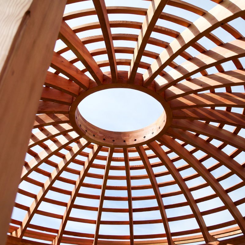 The Wooden Dome Pergola (Options: 16' Diameter, with Deck in Coffee Stain, Douglas-fir, Open Roof with Slats at 6", 9' Posts, No Electrical Wiring Trim, 6-Post Anchor Kit for Concrete, Transparent Premium Sealant). Photo Also shows a Round Picnic Table and a Rory's Swing Set in Background. The Wooden Dome Pergola (Options: 16' Diameter, with Deck in Coffee Stain, Douglas-fir, Open Roof with Slats at 6", 9' Posts, No Electrical Wiring Trim, 6-Post Anchor Kit for Concrete, Transparent Premium Sealant). Photo Also shows a Round Picnic Table and a Rory's Swing Set in Background.