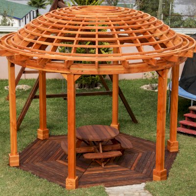 The Wooden Dome Pergola (Options: 16' Diameter, with Deck in Coffee Stain, Douglas-fir, Open Roof with Slats at 6", 9' Posts, No Electrical Wiring Trim, 6-Post Anchor Kit for Concrete, Transparent Premium Sealant). Photo Also shows a Round Picnic Table and a Rory's Swing Set in Background.