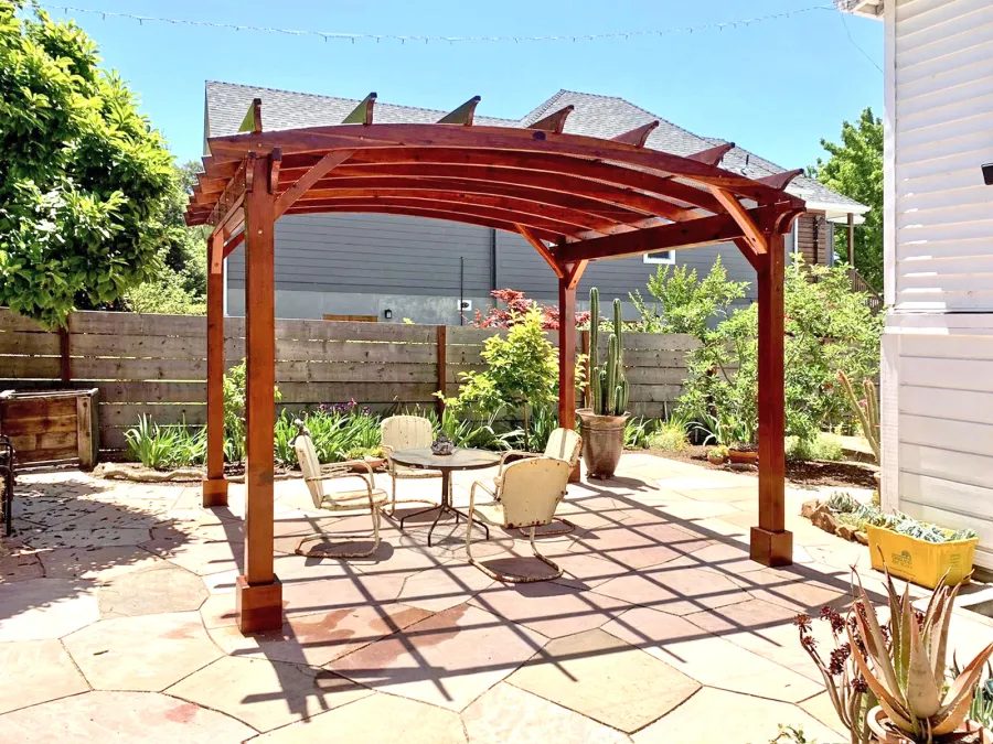 Arched Open Sky Pergolas (Options: 12' L x 14' Arc W, California Redwood, 1 Electrical Wiring Trim, 4-Post Anchor Kit for Concrete, No Ceiling Fan Base, No Privacy Panels, No Curtain Rods, 9.5' Post Height, Transparent Premium Sealant). Custom decorative steel shading added by customer. Photo was taken one year after installation. Photo Courtesy of K. Cates of Oajland, California.