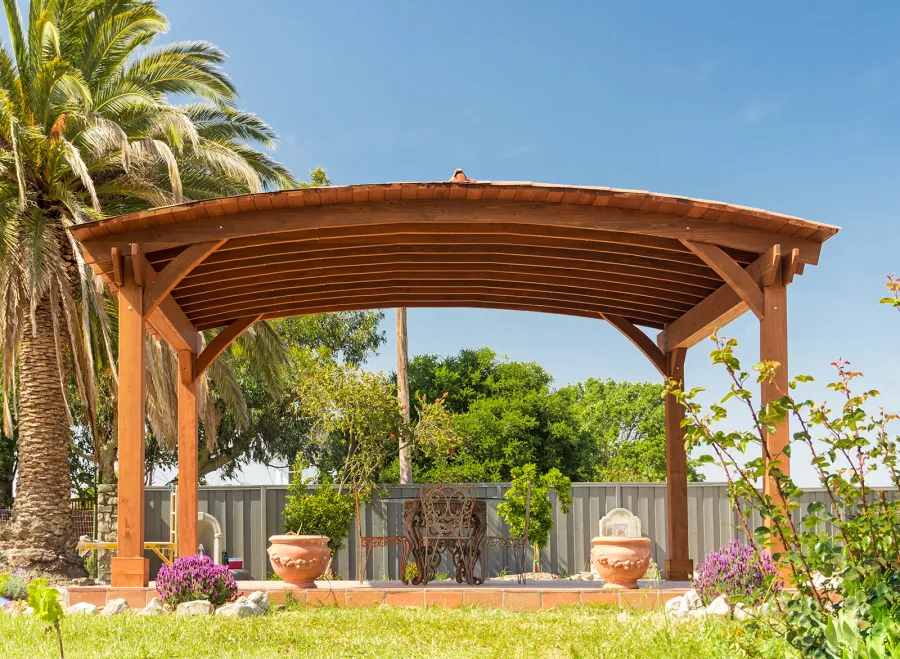 Custom Arched Thick Timber Pavilion (Options: 14' L x 20' Arc W, Mature Redwood, 1 Electrical Wiring Trim, 4-Post Anchor Kit for Concrete, No Ceiling Fan Base, No Privacy Panel, No Curtain Rods, 9 ft H, with 2x6's Roof Boards by Custom Request, Coffee-Stain Premium Sealant). Photo Courtesy of Siino Ventures of Kikrland, Washington.