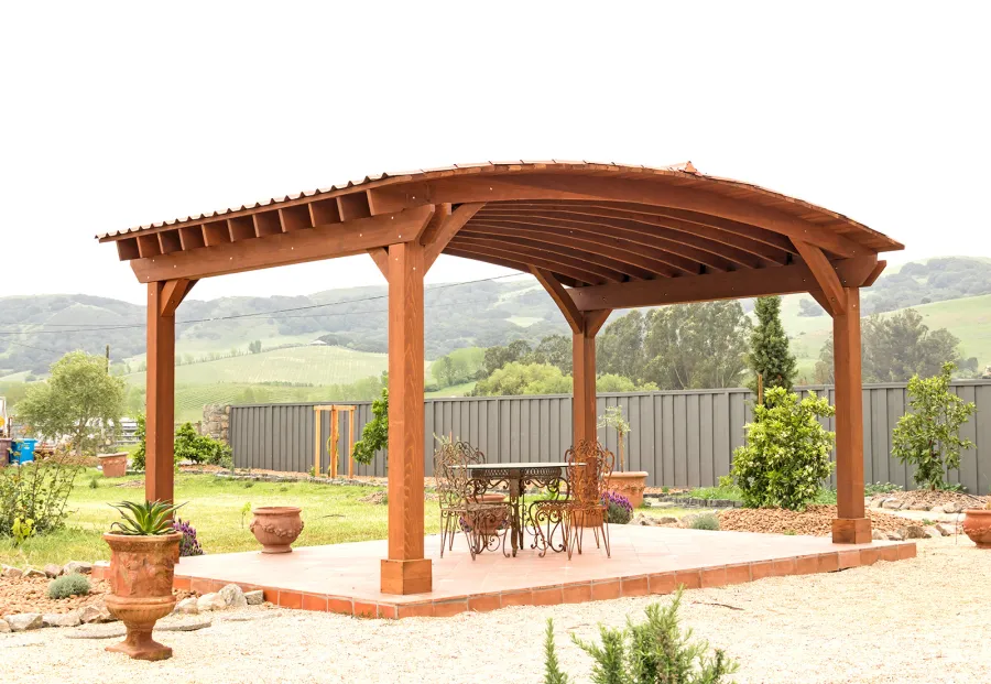 Custom Arched Thick Timber Pavilion (Options: 14' L x 20' Arc W, Mature Redwood, 1 Electrical Wiring Trim, 4-Post Anchor Kit for Concrete, No Ceiling Fan Base, No Privacy Panel, No Curtain Rods, 9 ft H, with 2x6's Roof Boards by Custom Request, Coffee-Stain Premium Sealant). Photo Courtesy of Siino Ventures of Kikrland, Washington.