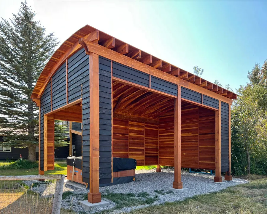 Custom  Arched Thick Timber Pavilion (Options: 28' L x 18' Arc W, California Redwood, Post Anchor Kit for High-Wind, with Custom Privacy Walls, 10' & 12' H Posts, No Curtain Rods, Walls Siding with Black Stain and the Rest of the Structure with Transparent Premium Sealant). Photo Courtesy of D. Harris of Tetonia, ID.
