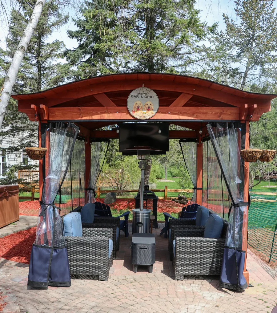 Custom Backyard Pavilion Kit with Extra Supports and Braces on Arches Side (Options: 16' L x 12' Arc W, Douglas-fir, 1 Post Electrical Wiring Trim, 4-Post Anchor Kit for High-Wind, 1 TV Mount Base by Custom Request, No Privacy Panels, No Curtain Rods, 9 ft Post Height, Cherry-Stain Premium Sealant). Photo Courtesy of E. Chen of Ann Arbor, Michigan.