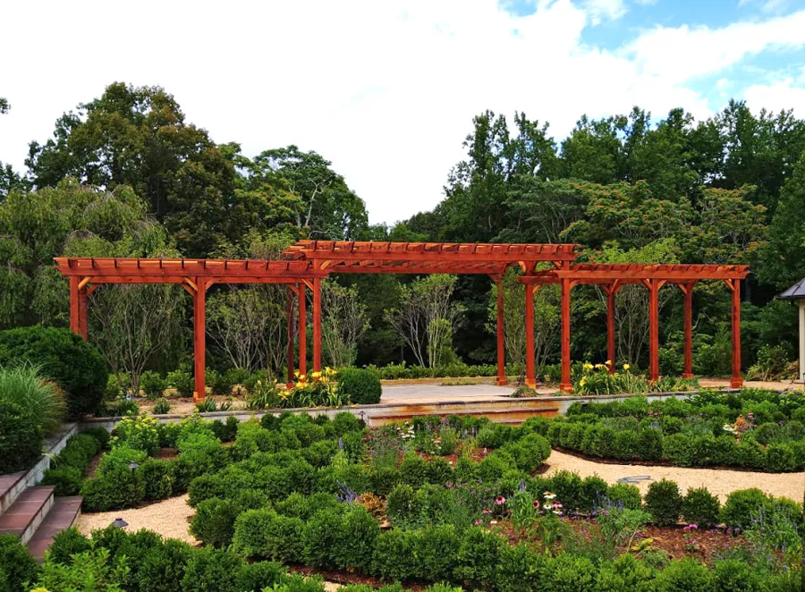 Custom Wooden Pergola (Options: 56' L [20' W in Central Section and 8' W on Sides], Mature Redwood, No Electrical Wiring Trim, 14-Post Anchor Kit for Concrete, No Ceiling Fan Base, No Privacy Panels, No Curtain Rods, Transparent Premium Sealant). Photo Courtesy of J. Kelly of Crozet, Virginia.