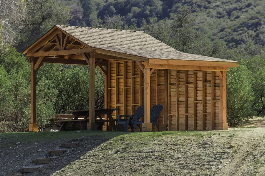 Custom Del Norte Outdoor Kitchen Pavilion (Options: 12' L x 12' W, with 9' x 12' Shed Pavilion Attached, Douglas-fir, 6-Post Anchor Kit for High-Wind, No Ceiling Fan Base, No Electrical Wiring Trim Kit, No Post Decorative Trims, with Custom Solid Wall, Transparent Premium Sealant). Photo Courtesy of J. Randall of Warner Springs, CA.