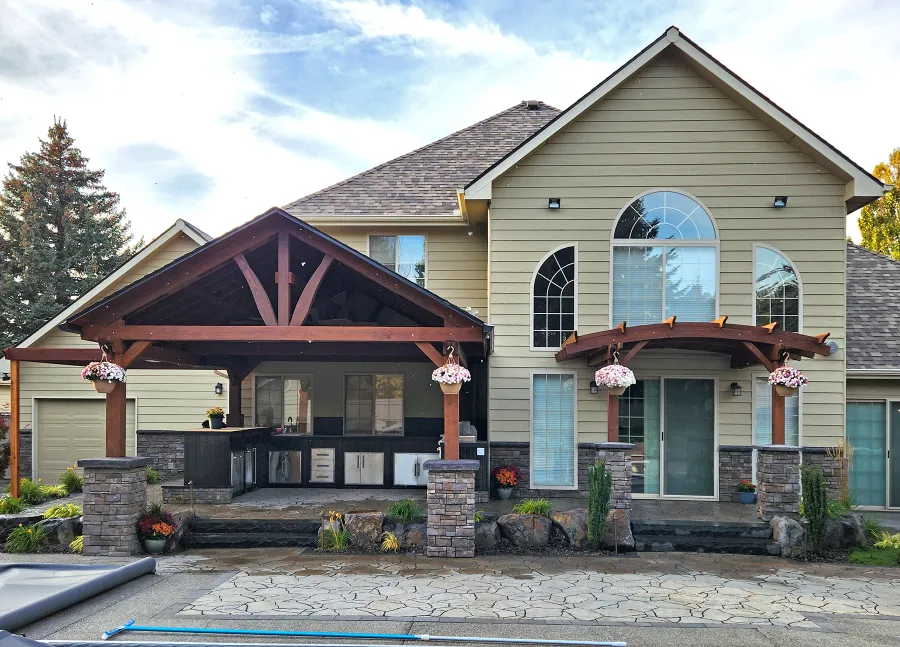 Del Norte Outdoor Kitchen Pavilion (Options: 19.5' L x 17' W, Mature Redwood, No Privacy Panel, Post Anchor Kit for High Wind, 10.5' H Posts, 1 Ceiling Fan Base, Electrical Wiring Trim for 2 Posts, No Curtain Rod, Coffee-Stain Premium Sealant). Photo Also Shows a 12' x 12' Attached Arched Pergola. Photo Courtesy of Elements Landscaping of Hayden, ID.