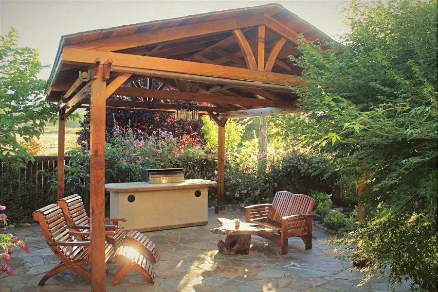 Del Norte Outdoor Kitchen Pavilion (Options: 16' L x 19' W, California Redwood, 4-Post Anchor Kit for Concrete, 4 Curtain Rods, No Ceiling Fan Base, Electrical Wiring Trim Kit for 2 Posts, Transparent Premium Sealant). Photo also shows a Loveseat and two Ensenada Easychairs with Ottoman. Photo Courtesy of D. Leetz of Petaluma, CA.