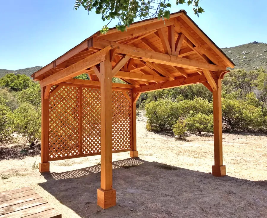 Del Norte Outdoor Kitchen Pavilion (Options: 12' L x 12' W, 1 Full Wall Lattice Privacy Panel, Douglas-fir, 4-Post Anchor Kit for High-Wind, No Ceiling Fan Base, No Electrical Wiring Trim Kit, Straight Internal Truss Supports by Custom Request, No Post Decorative Trims, Transparent Premium Sealant). Photo Courtesy of J. Randall of Warner Springs, CA.