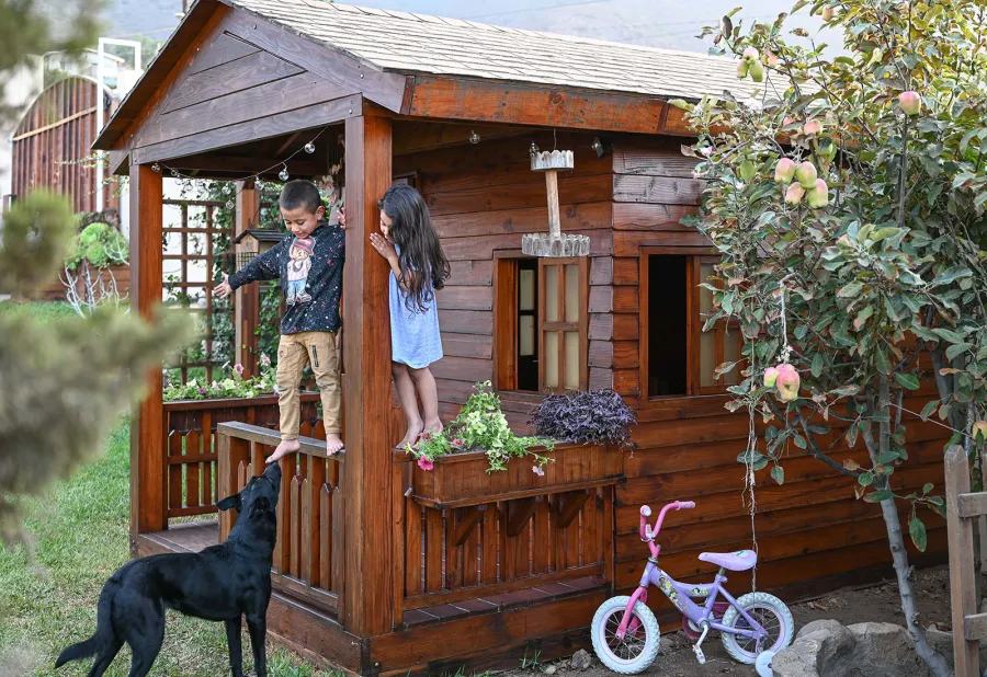 Kid's The Backyard Cabin (Options: 12ft L x 8ft W, 7ft Wall H, Douglas-Fir, 4ft Front Porch Size [Included in the Overall Length], Interior Decking, Transparent Premium Sealant). Photo shows structure recently resealed after 6 years of loving service.