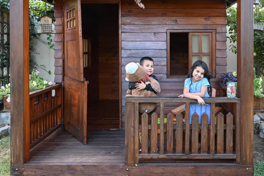 Kid's Backyard Cabin (Options: 12ft L x 8ft W, 7ft Wall H, Douglas-Fir, 4ft Front Porch Size [Included in the Overall Length], Interior Decking, Transparent Premium Sealant). Photo shows structure recently resealed after 6 years of loving service.