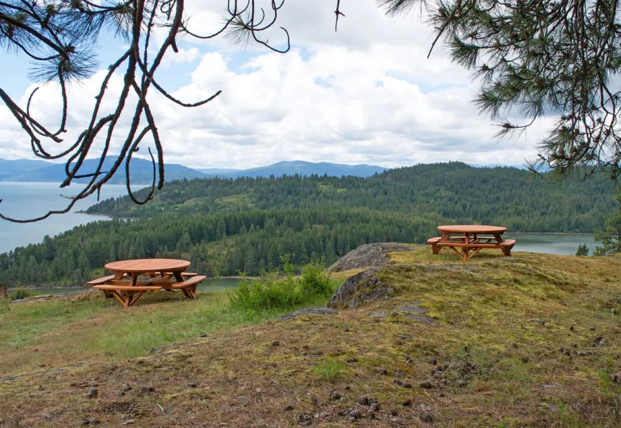 Round Wooden Picnic Tables (Attached Benches) (Options: 6' Diameter, Attached Benches, California Redwood, Standard Tabletop, No Lazy Susan, Umbrella Hole & Plug, Transparent Premium Sealant). These beautiful tables are installed at the “Bull Pine Ledge”, looking out on Lake Pend Orielle from Cloudsledge Conservation Trust, Hope Idaho. Photo Courtesy of Art Green.