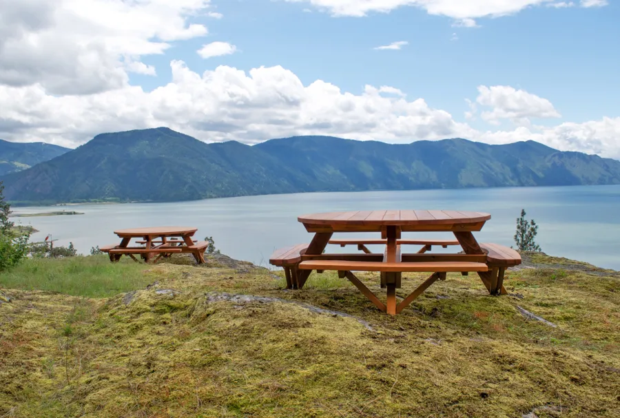 Round Wooden Picnic Tables (Attached Benches) (Options: 6' Diameter, Attached Benches, California Redwood, Standard Tabletop, No Lazy Susan, Umbrella Hole & Plug, Transparent Premium Sealant). These beautiful tables are installed at the “Bull Pine Ledge”, looking out on Lake Pend Orielle from Cloudsledge Conservation Trust, Hope Idaho. Photo Courtesy of Art Green.