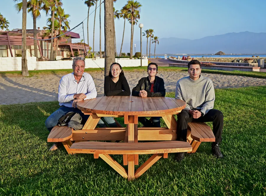 Round Wooden Picnic Table (Attached Benches) (Options: 5' Diameter, Attached Benches, Mosaic Douglas-Fir, Standard Tabletop, No Lazy Susan, 2" Umbrella Hole, Transparent Premium Sealant). Photo courtesy of El Estero Beach Resort in Ensenada, Mexico.