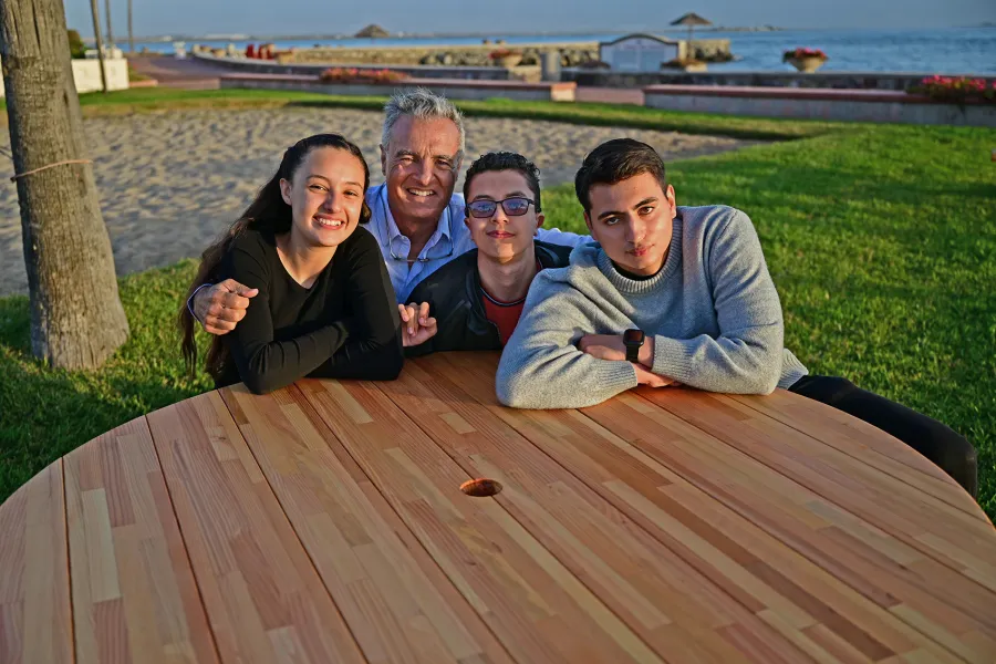 Round Wooden Picnic Table (Attached Benches) (Options: 5' Diameter, Attached Benches, Mosaic Douglas-Fir, Standard Tabletop, No Lazy Susan, 2" Umbrella Hole, Transparent Premium Sealant). Photo courtesy of El Estero Beach Resort in Ensenada, Mexico.