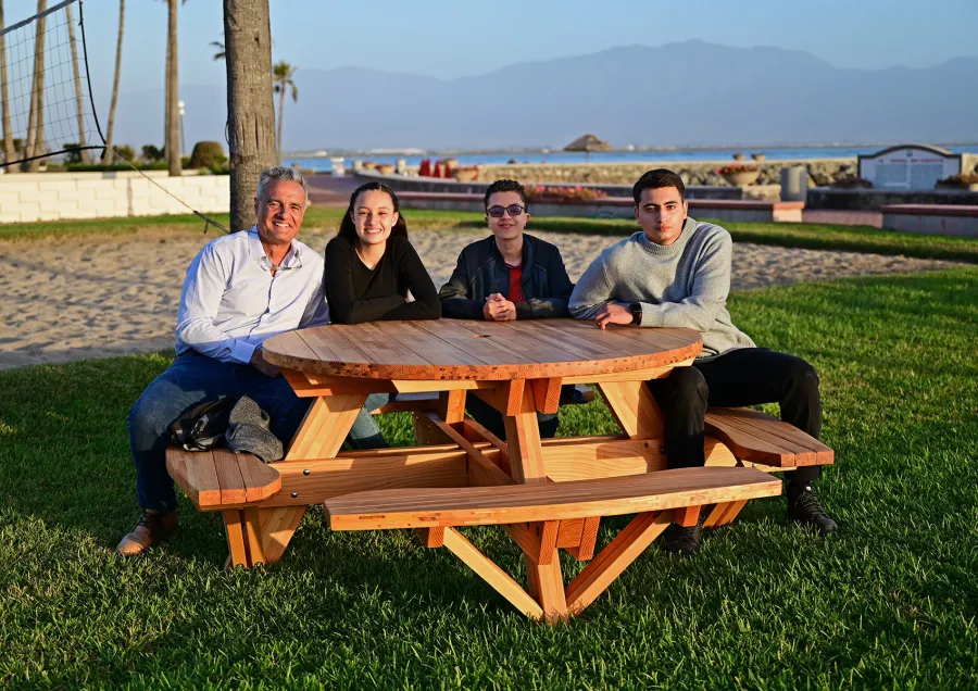 Round Wooden Picnic Table (Attached Benches) (Options: 5' Diameter, Attached Benches, Mosaic Douglas-Fir, Standard Tabletop, No Lazy Susan, 2" Umbrella Hole, Transparent Premium Sealant). Photo courtesy of El Estero Beach Resort in Ensenada, Mexico.