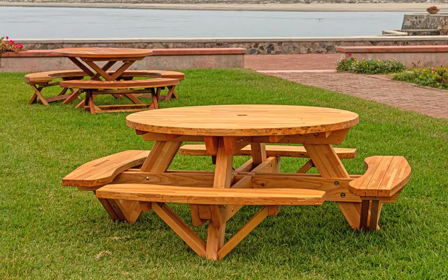Round Wooden Picnic Table (Attached Benches) (Options: 5' Diameter, Attached Benches, Mosaic Douglas-Fir, Standard Tabletop, No Lazy Susan, 2" Umbrella Hole, Transparent Premium Sealant). Photo Shown a Kary's Folding Table Set in the Background. Photo courtesy of El Estero Beach Resort in Ensenada, Mexico.