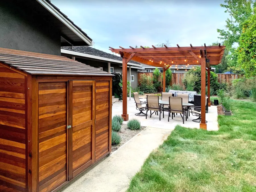Storage Sheds (Options: 7' W, 4.5' D, 7' H, California Redwood, Single Door, One Shelf on the Side Opposite the Door, 42" H, Transparent Premium Sealant). Photo Also Shows a Garden Pergola in the Background. Photo Courtesy of J. Lewis of Mountain View, CA.