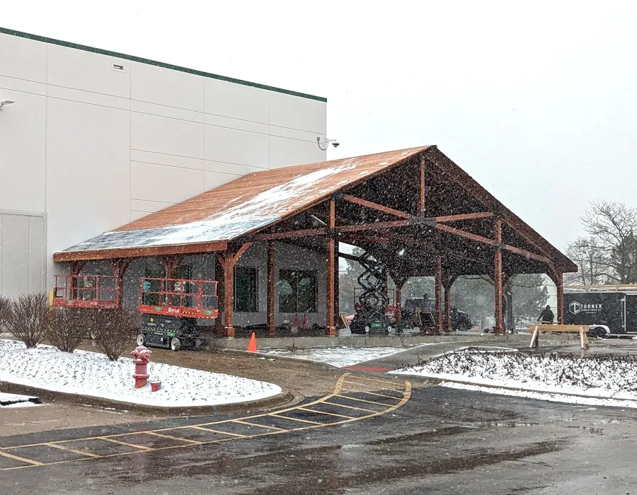 Esther Scissor Truss Pavilion (Options: 33’ L x 63’ W, California Redwood, Standard 3/4" T&G Roof Boards, 16' and 10' H Posts by Custom Request, with 4 Ceiling Fan Bases, High-Wind Post Anchors, 5:12 Roof Pitch, Transparent Premium Sealant). Installation in Process, Photo Shows the Final Roofing Only Partially Installed. Photo Courtesy of the HelloFresh Produce Company of Bolingbrook, IL.