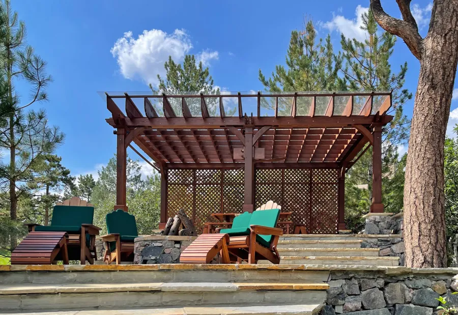 Montvale Pergolas (Options: 24' x 16', Mature Redwood, 6-Post Anchor Kit for Concrete, 1 Ceiling Fan Base and 1 T.V. Base, 2 Curtain Rods, 1 Lattice Privacy Panel, 9.5' H Posts, with Rain Guard, Coffee-Stain Premium Sealant). Photo Also Shows Some Adirondack Chairs with Ottoman. Photo Taken 1 Year After Installation, and After Restaining. Photo Courtesy of J. Brinkman of Castle Rock, Colorado.