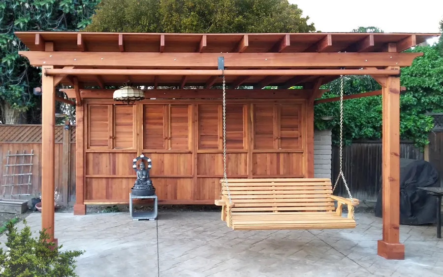 Sunset Patio Pavilion (Options: 18' x 14', 1 Shutter Privacy Panel [Top] with Solid Wall [Bottom], Mature Redwood, 9ft H, No Electrical Wiring Trim, 4-Post Anchor Kit for High-Wind, No Ceiling Fan Base, 3 Curtain Rods, Transparent Premium Sealant). The Photo Also Shows a Large Bench Swing Seat in Douglas-fir, Ensenada Seat Style.