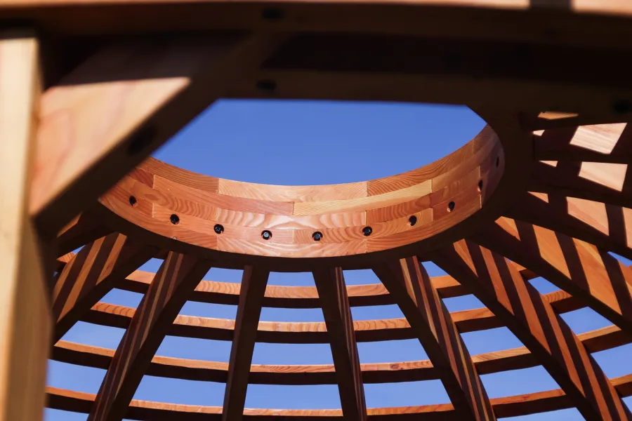 Wooden Dome Pergola (Options: 16' Diameter, with Deck in Coffee Stain, Douglas-fir, Open Roof with Slats at 6", 9' Posts, No Electrical Wiring Trim, 6-Post Anchor Kit for Concrete, Transparent Premium Sealant). Photo Also shows a Round Picnic Table and a Rory's Swing Set in Background.
